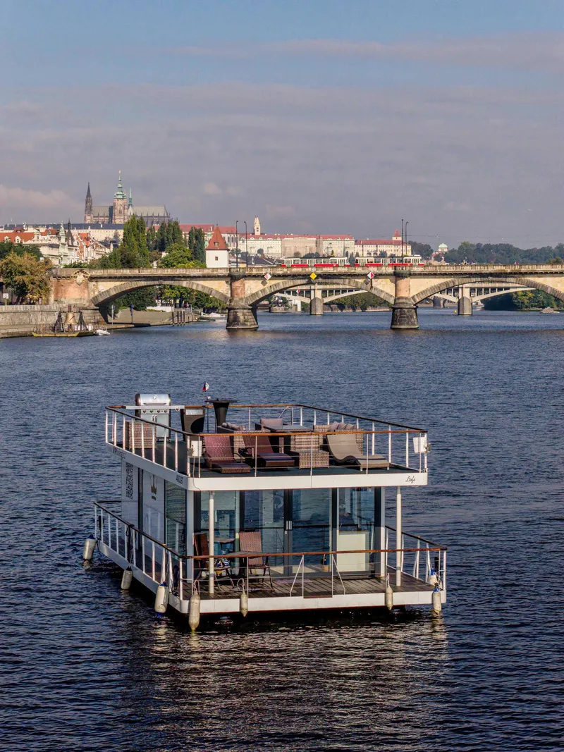 Houseboat VIP Living na Vltavě, v pozadí kamenný most s tramvají a Pražský hrad